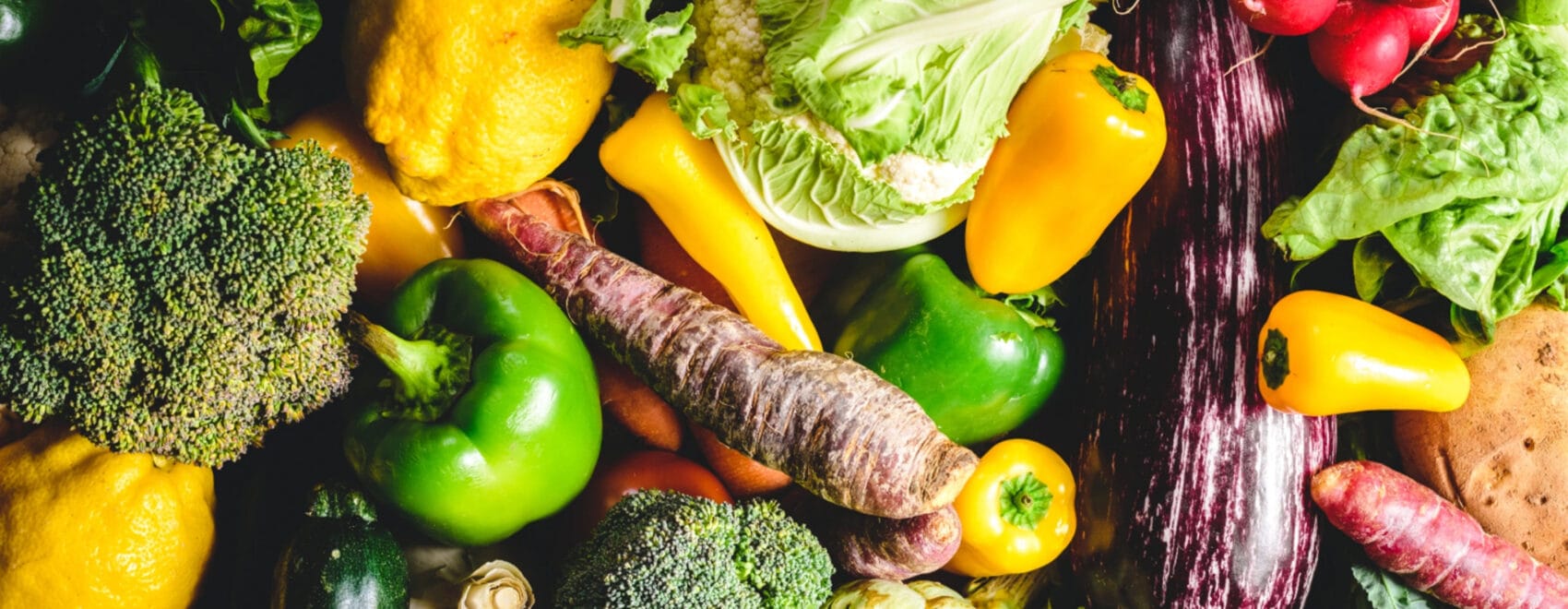 a pile of various vegetables such as lettuce, green and yellow bell peppers, and broccoli